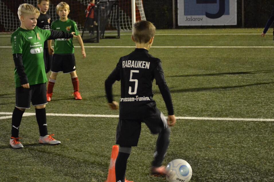Junge in schwarzem Trikot mit der Nummer 5 dribbelt einen Fußball auf einem Kunstrasenfeld, umgeben von anderen Spielern.