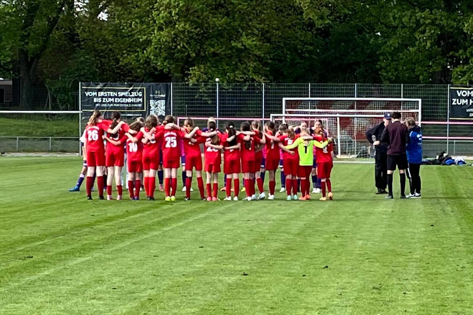 Frauenfußballmannschaft in roten Trikots steht im Kreis auf dem Platz, um sich vor einem Spiel zu besprechen.