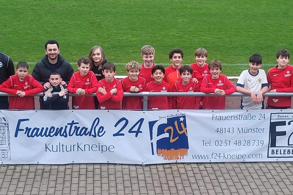 Gruppennfoto von Kindern und Trainern in roten Trikots vor einem Banner der Kulturkneipe Frauenstra&szlig;e 24.
