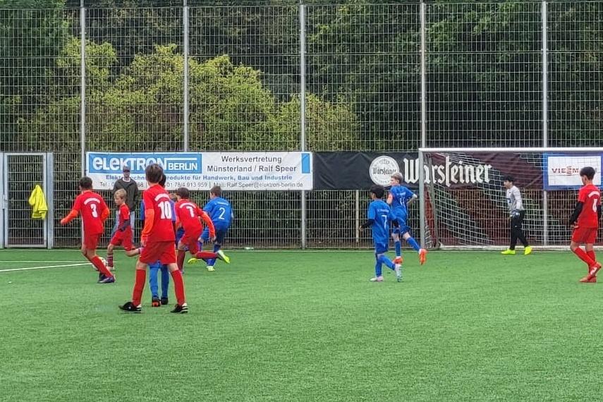 Jugend-Fußballspiel auf einem Kunstrasenplatz mit Spielern in roten und blauen Trikots, Torwart im Hintergrund.