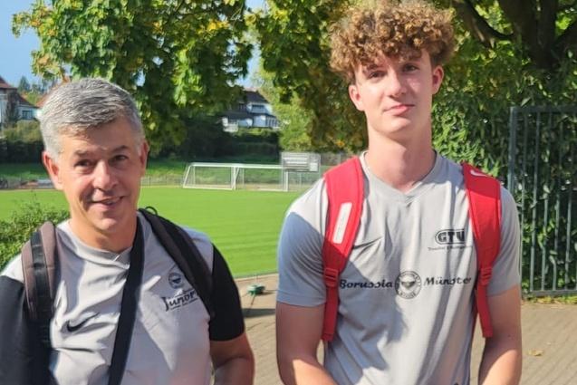 Zwei M&auml;nner in Sportkleidung stehen zusammen im Freien, der &auml;ltere mit einer K&uuml;hltasche und der j&uuml;ngere mit einem Rucksack.