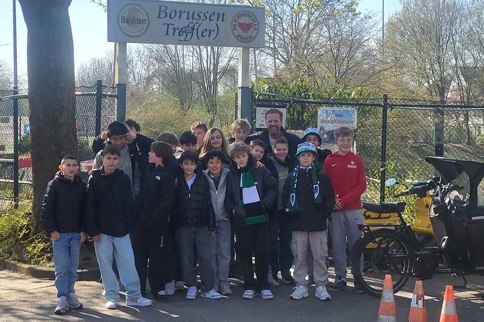 Gruppe von Jugendlichen steht vor dem &bdquo;Borussen Treff&ldquo; mit einem Fahrrad und Verkehrskegeln im Vordergrund.