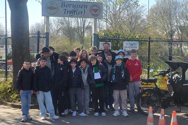 Gruppe von Jugendlichen steht vor dem &bdquo;Borussen Treff&ldquo; mit einem Fahrrad und Verkehrskegeln im Vordergrund.