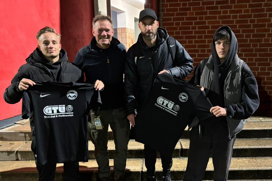 Vier Personen stehen auf einer Treppe vor einem roten Hintergrund und halten schwarze T-Shirts mit dem Aufdruck „CTU“ in der Hand.