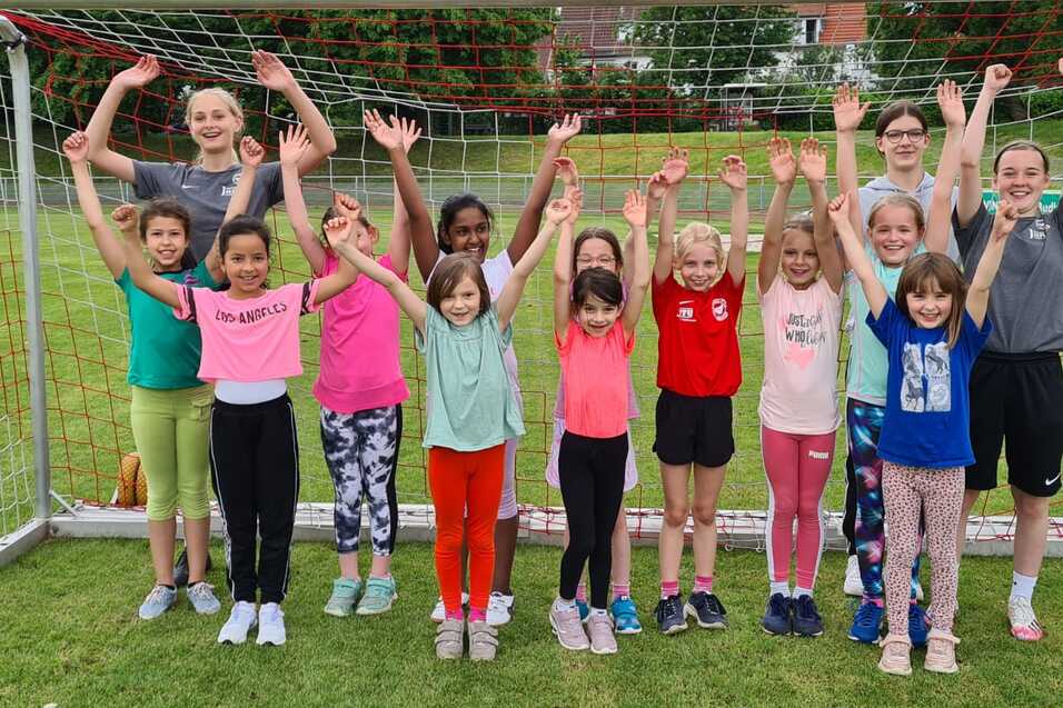 Gruppe von Mädchen und Frauen feiert vor einem Fußballtor, alle heben die Arme in die Luft.