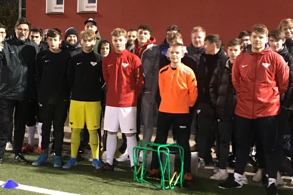 Gruppe von Fußballspielern in Trainingskleidung posiert vor einer Sportanlage bei Dämmerung.