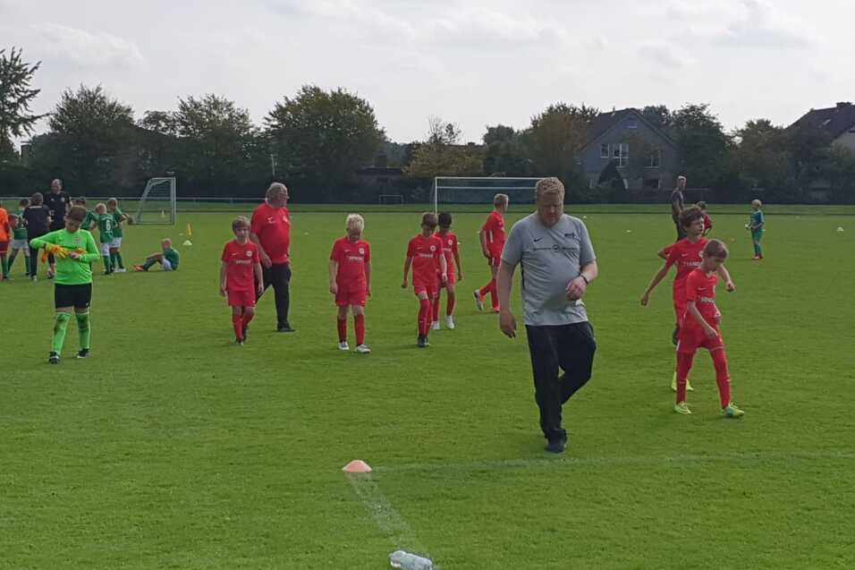 Fu&szlig;ballmannschaft in roten Trikots joggt auf einem gr&uuml;nen Spielfeld, w&auml;hrend Trainer sie anleitet.