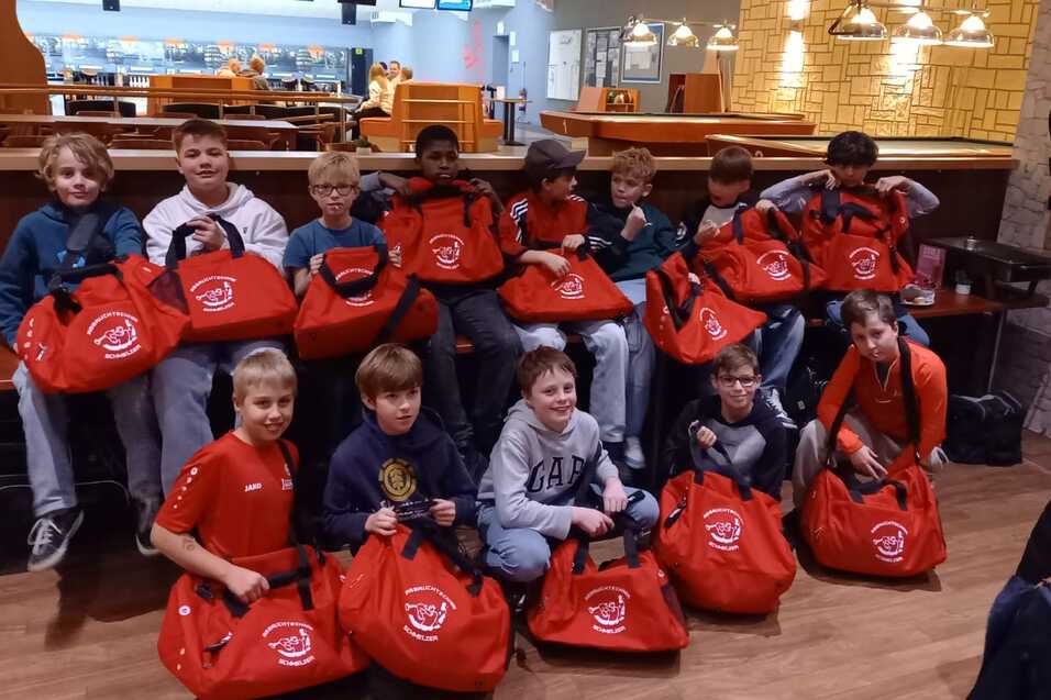 Gruppe von Jungen sitzt mit roten Sporttaschen in einem Bowling-Café, im Hintergrund sind Bowlingbahnen sichtbar.