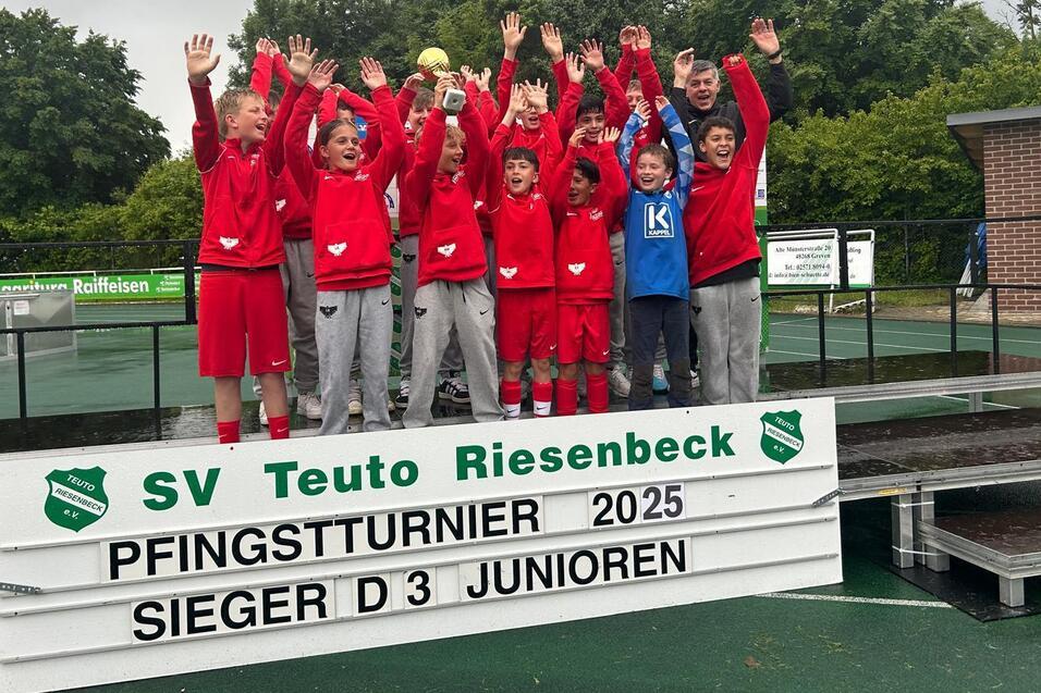Gruppe junger Fußballspieler in roten Trikots feiert auf einem Siegertreppchen beim Pfingstturnier 2025.