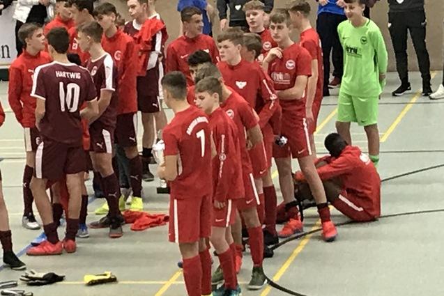 Gruppe von Jugendlichen in roten Fu&szlig;balltrikots versammelt auf einem Sportplatz, einige bereiten sich auf ein Spiel vor.