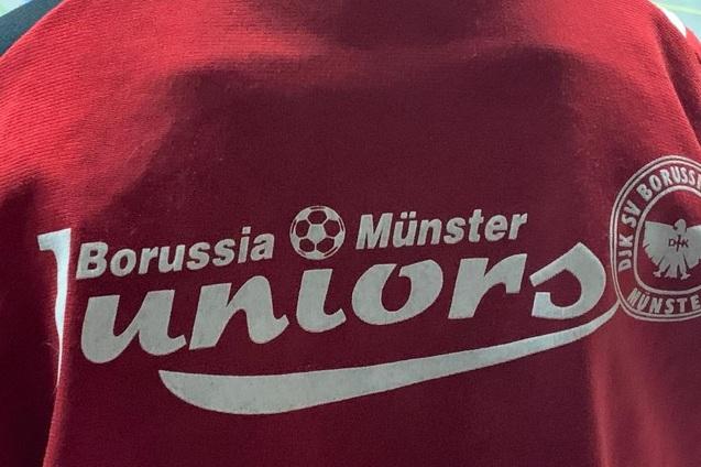 R&uuml;ckansicht eines roten T-Shirts mit dem Aufdruck &bdquo;Borussia M&uuml;nster Juniors&ldquo; und Vereinslogo.