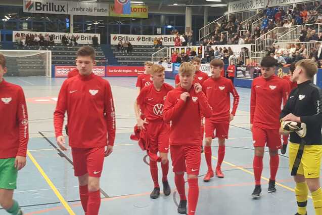 Gruppe von Jugendlichen in roten Sportanz&uuml;gen betritt eine Halle, im Hintergrund Zuschauer auf Trib&uuml;nen.