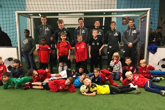 Gruppenfoto von Jungen in Sportkleidung vor einem Fu&szlig;balltor in einer Halle, einige liegen auf dem Rasen, andere stehen.