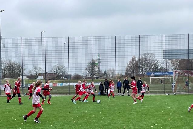 Mannschaftssport auf einem Fu&szlig;ballplatz mit mehreren Spielerinnen in roten Trikots, die um den Ball k&auml;mpfen.