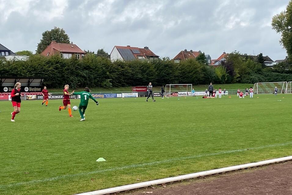 Ein Fußballspiel mit Spielern in roten und grünen Trikots auf einem Rasenplatz, im Hintergrund Tore und Zuschauer.