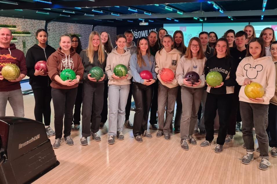 Gruppencollage von 20 Personen in einem Bowling-Center, jede mit einer bunten Bowlingkugel in der Hand.