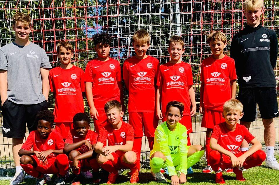 Gruppe von zehn jungen Fu&szlig;ballspielern in roten Trikots, posierend vor einem Fu&szlig;balltor auf einem gr&uuml;nen Platz.