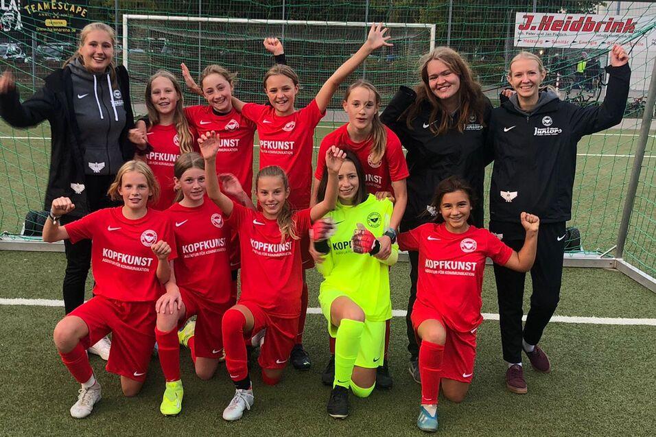 Gruppenfoto eines Fußballteams aus Mädchen in roten Trikots, posierend vor einem Tor auf einem Rasensportplatz.