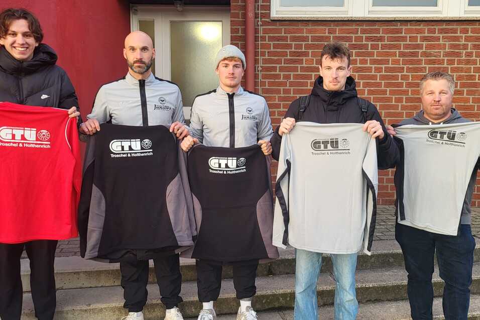 Fünf Personen stehen auf einer Treppe und halten verschiedene T-Shirts mit dem Logo „GTU“ in schwarz, rot und grau.