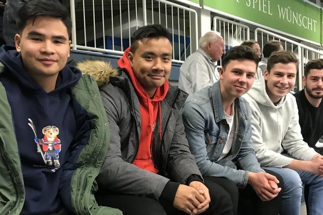 F&uuml;nf junge M&auml;nner sitzen nebeneinander in einer Trib&uuml;ne, jeder in unterschiedlichen Freizeitoutfits.