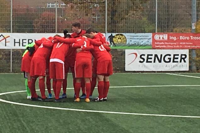Fu&szlig;ballteam in roten Trikots bildet einen Kreis auf dem Platz und bereitet sich auf das Spiel vor.