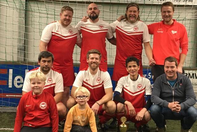 Gruppenfoto einer Fu&szlig;ballmannschaft mit Pokal, bestehend aus sechs Spielern und zwei Kindern im Vordergrund.