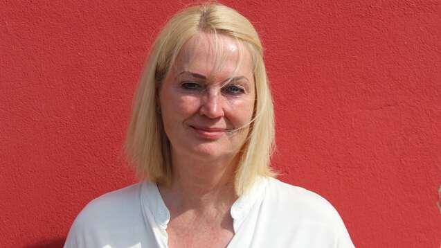 Frau mit blonden Haaren in wei&szlig;em Oberteil steht vor roter Wand.