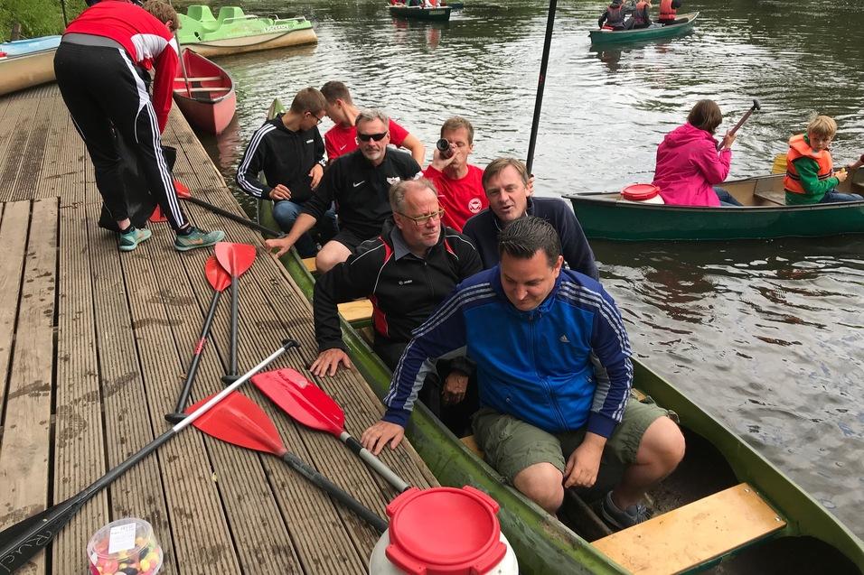 Gruppe von sechs Personen sitzt in einem Kanu an einem Steg, w&auml;hrend andere Boote im Hintergrund fahren.