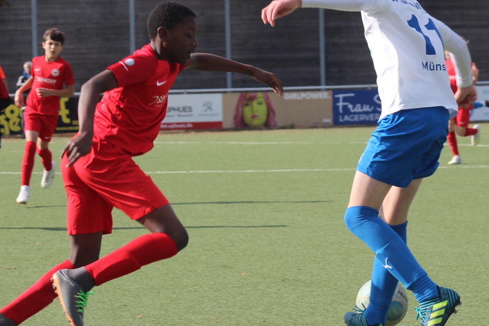 Zwei Jugend-Fu&szlig;ballspieler in rot und blau dribbeln den Ball auf einem Kunstrasenplatz im Spiel.