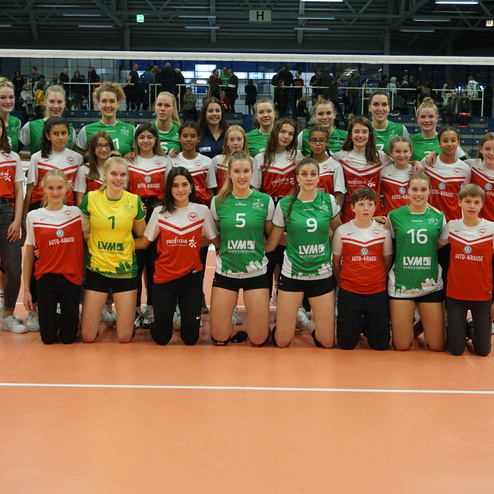 Gruppenfoto von zwei Volleyballmannschaften mit Spielerinnen in roten und gr&uuml;nen Trikots auf einem Volleyballfeld.