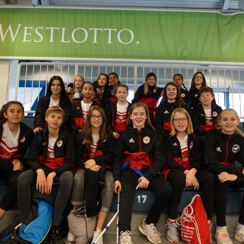 Gruppe von Jugendlichen in Sportjacken sitzt auf Trib&uuml;ne, l&auml;chelnd und in angeregter Gespr&auml;chsweise.