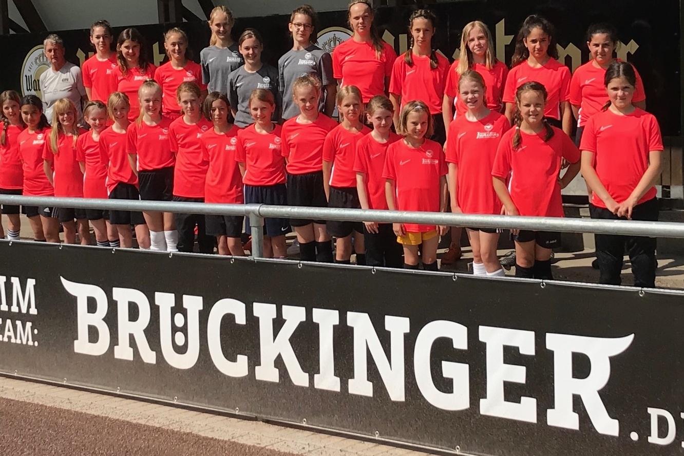 Mannschaftsfoto von M&auml;dchen in roten Trikots vor einer Werbebande mit dem Schriftzug &bdquo;BRUCKINGER&ldquo;.