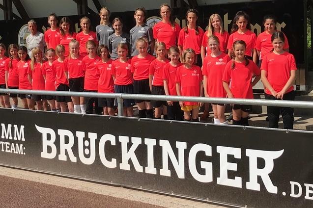 Mannschaftsfoto von M&auml;dchen in roten Trikots vor einer Werbebande mit dem Schriftzug &bdquo;BRUCKINGER&ldquo;.
