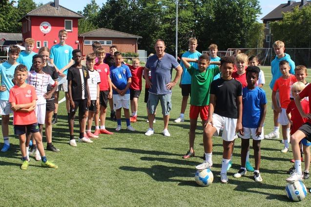 Gruppe von Jugendlichen in Sportkleidung auf einem Fu&szlig;ballplatz, um einen Trainer mit B&auml;llen versammelt.