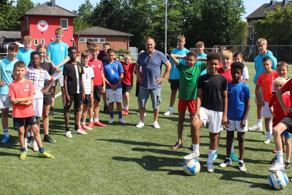 Gruppe von Jugendlichen in Sportkleidung auf einem Fu&szlig;ballplatz, um einen Trainer mit B&auml;llen versammelt.