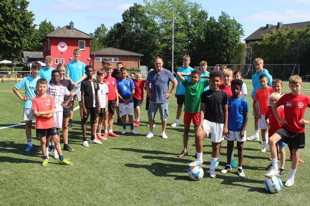 Gruppe von Jugendlichen in Sportkleidung auf einem Fu&szlig;ballplatz, um einen Trainer mit B&auml;llen versammelt.