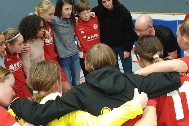 M&auml;dchenfu&szlig;ballmannschaft in einem huddle, Trainer erkl&auml;rt Taktik vor dem Spiel, alle tragen rote Trikots.