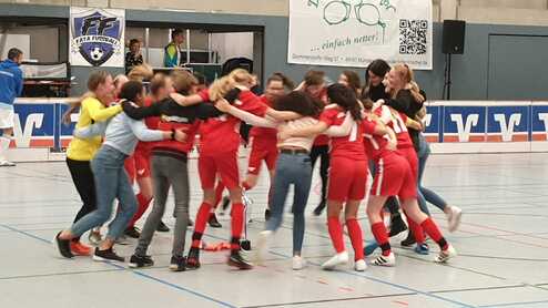 Gruppe junger Frauen in roten Trikots umarmt sich jubelnd in einer Sporthalle nach einem Spiel.