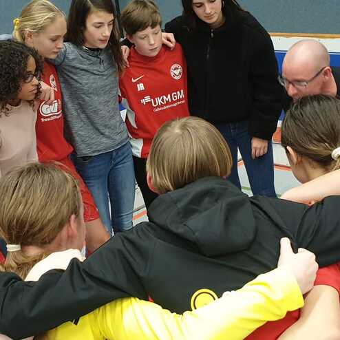 Mädchenfußballmannschaft in einem huddle, Trainer erklärt Taktik vor dem Spiel, alle tragen rote Trikots.