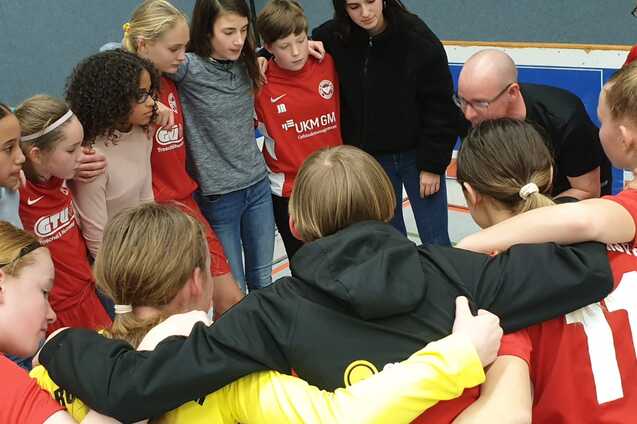 M&auml;dchenfu&szlig;ballmannschaft in einem huddle, Trainer erkl&auml;rt Taktik vor dem Spiel, alle tragen rote Trikots.