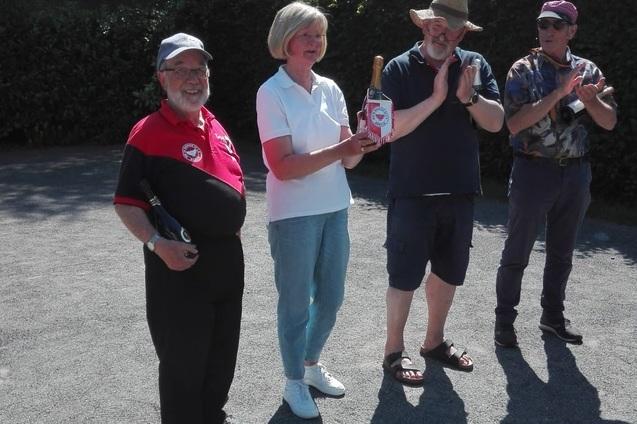 Vier Personen stehen im Freien und applaudieren, w&auml;hrend eine Frau einen Pokal in den H&auml;nden h&auml;lt.