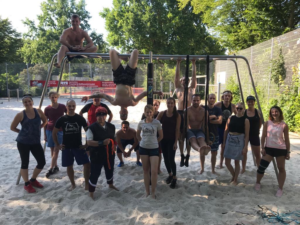 Gruppenzusammenkunft von 20 Personen auf einem Sandplatz, posierend an einem Spielger&auml;t im Freien.