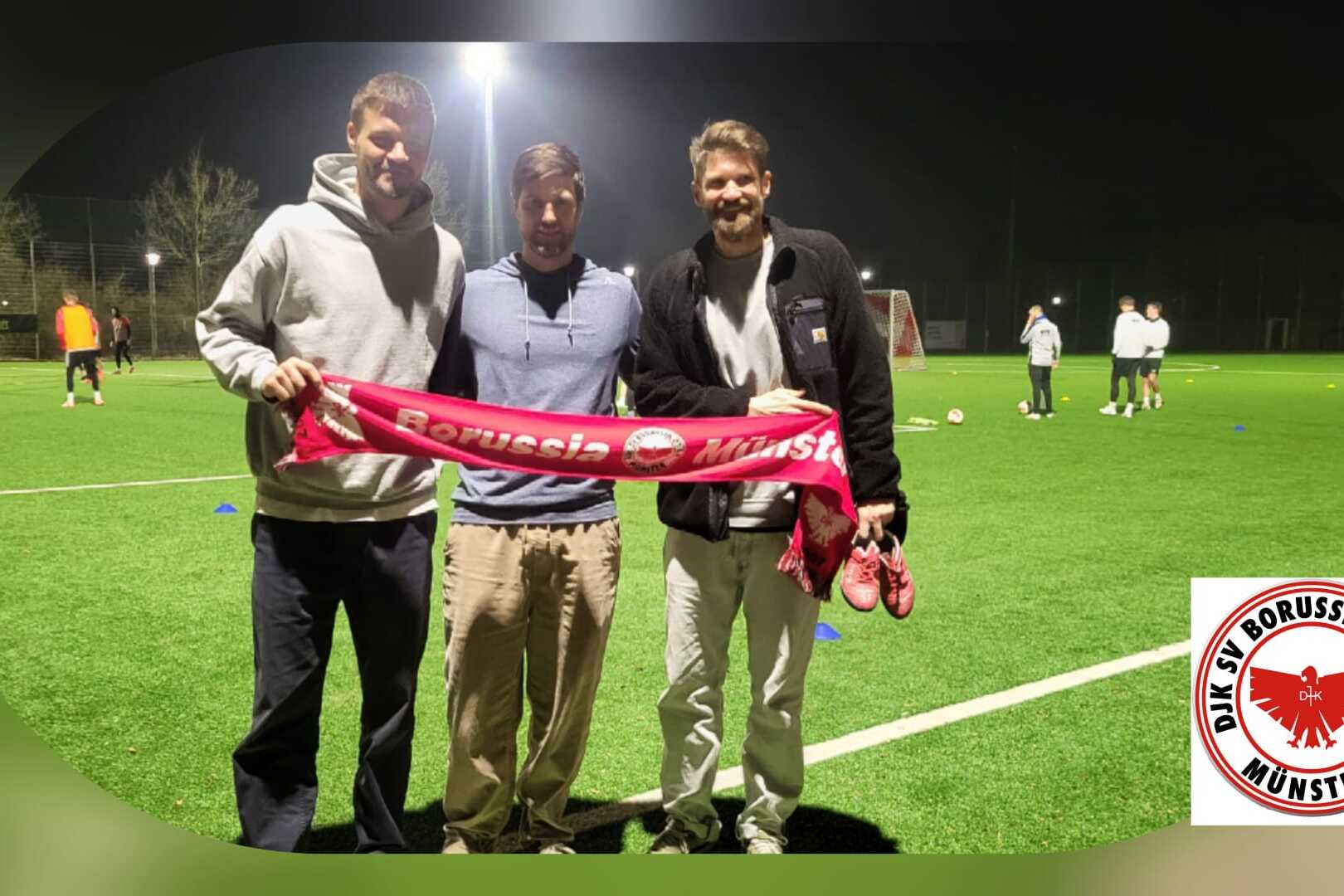 Drei M&auml;nner posieren auf einem Fu&szlig;ballplatz bei Nacht, halten ein rotes Banner von Borussia M&uuml;nster.
