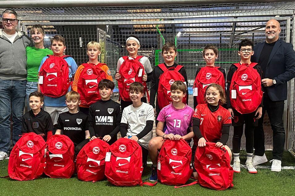 Gruppe von Kindern und Erwachsenen in einer Sporthalle, posierend vor einem Tor mit roten Rucks&auml;cken.