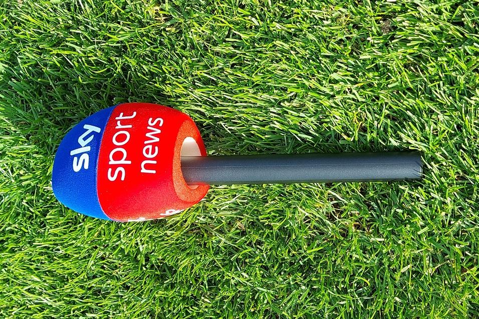 Sky Sport News Mikrofon auf einem Rasenfeld, mit blauem und rotem Kopf und einem schwarzen Griff.