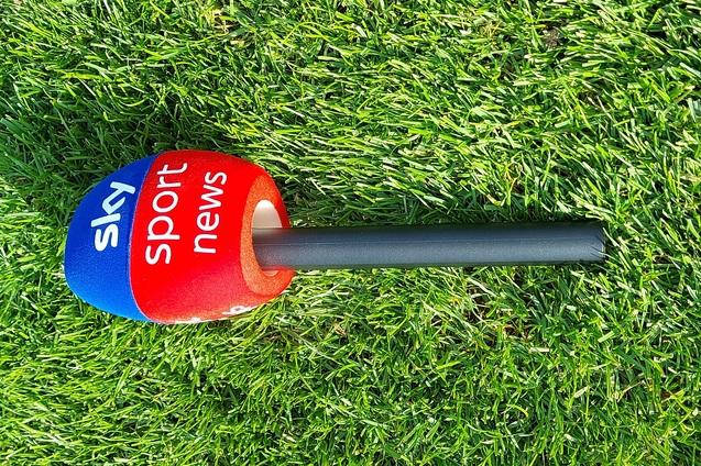 Sky Sport News Mikrofon auf einem Rasenfeld, mit blauem und rotem Kopf und einem schwarzen Griff.