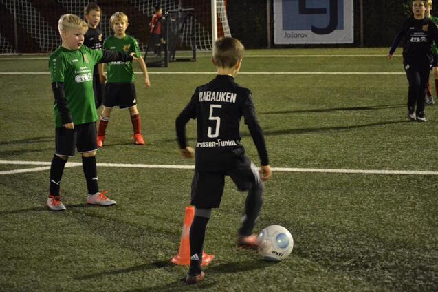 Junge in schwarzem Trikot mit der Nummer 5 dribbelt einen Fu&szlig;ball auf einem Kunstrasenfeld, umgeben von anderen Spielern.