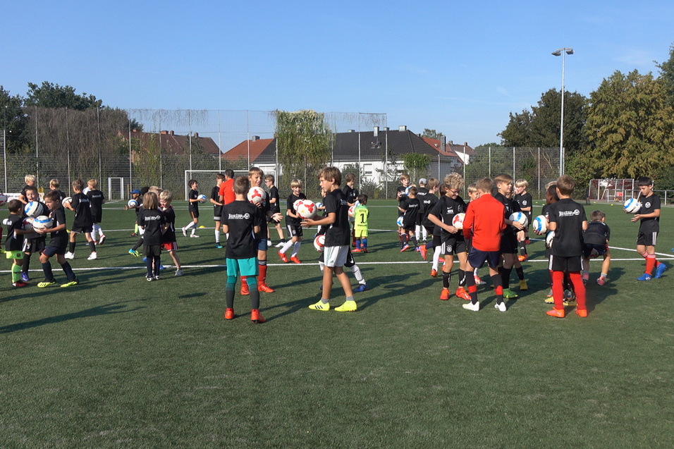 Gruppentraining von Kindern auf einem Fu&szlig;ballfeld mit Mitspielern in schwarzen Trikots und verschiedenen Shorts.