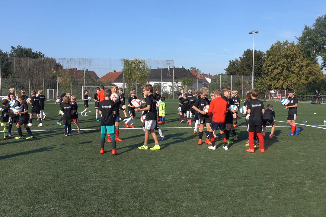 Gruppentraining von Kindern auf einem Fu&szlig;ballfeld mit Mitspielern in schwarzen Trikots und verschiedenen Shorts.