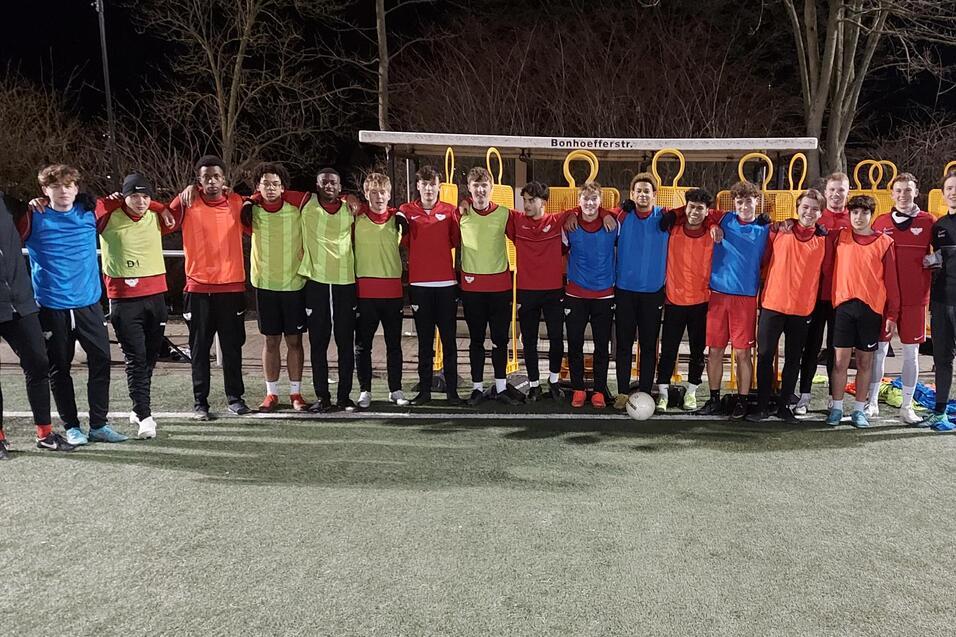 Gruppenzusammenstellung von 18 Fu&szlig;ballspielern in Trainingskleidung auf einem Kunstrasenplatz bei Nacht.